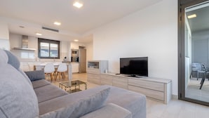Una sala moderna con un sofá gris, un televisor de pantalla plana y una mesa de centro de vidrio.