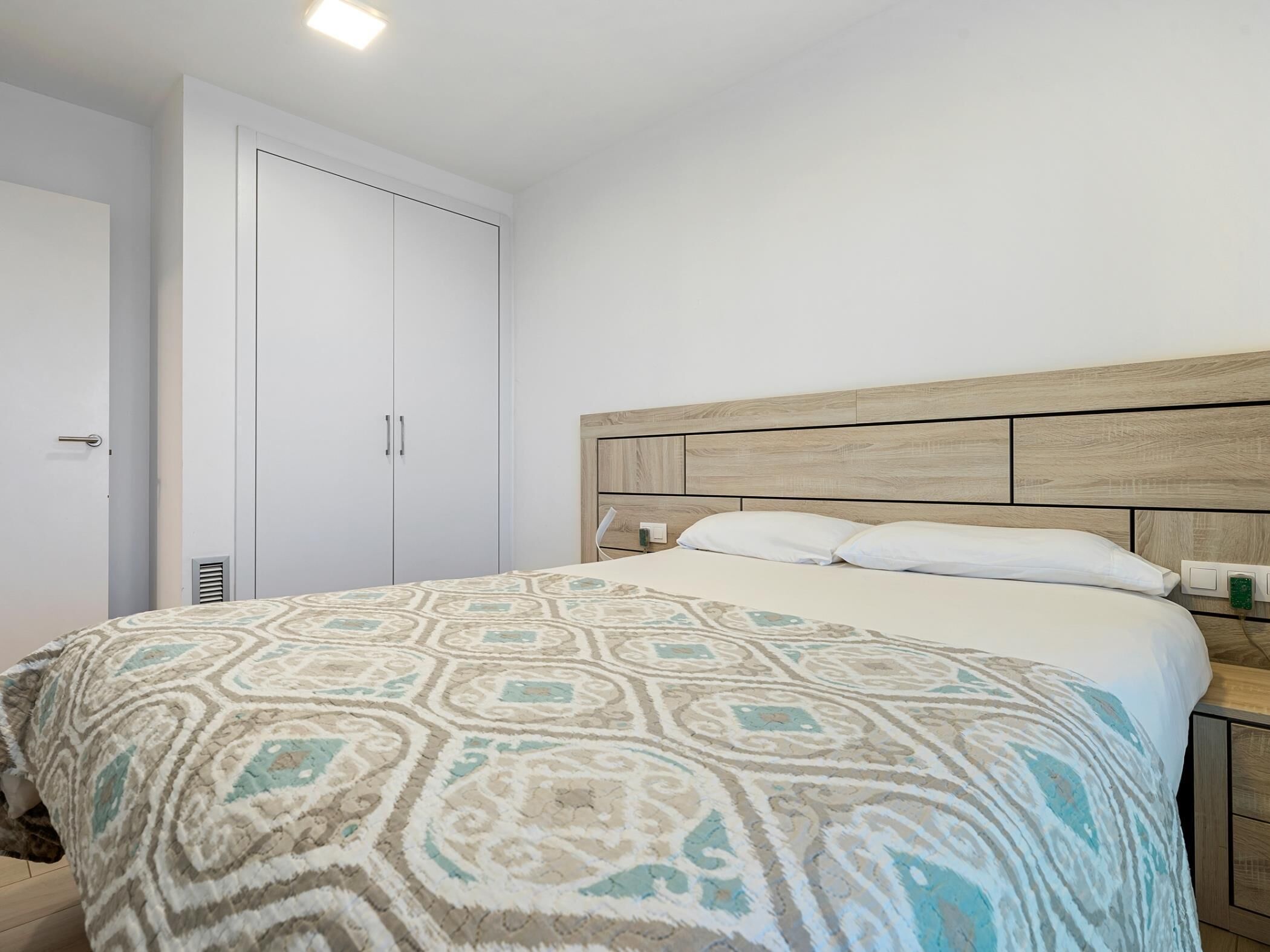 Quarto com cama, cabeceira de madeira, guarda-roupa e mesa de cabeceira com abajur.