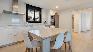 Una cocina moderna con armarios blancos, una mesa de comedor de madera y cuatro sillas.