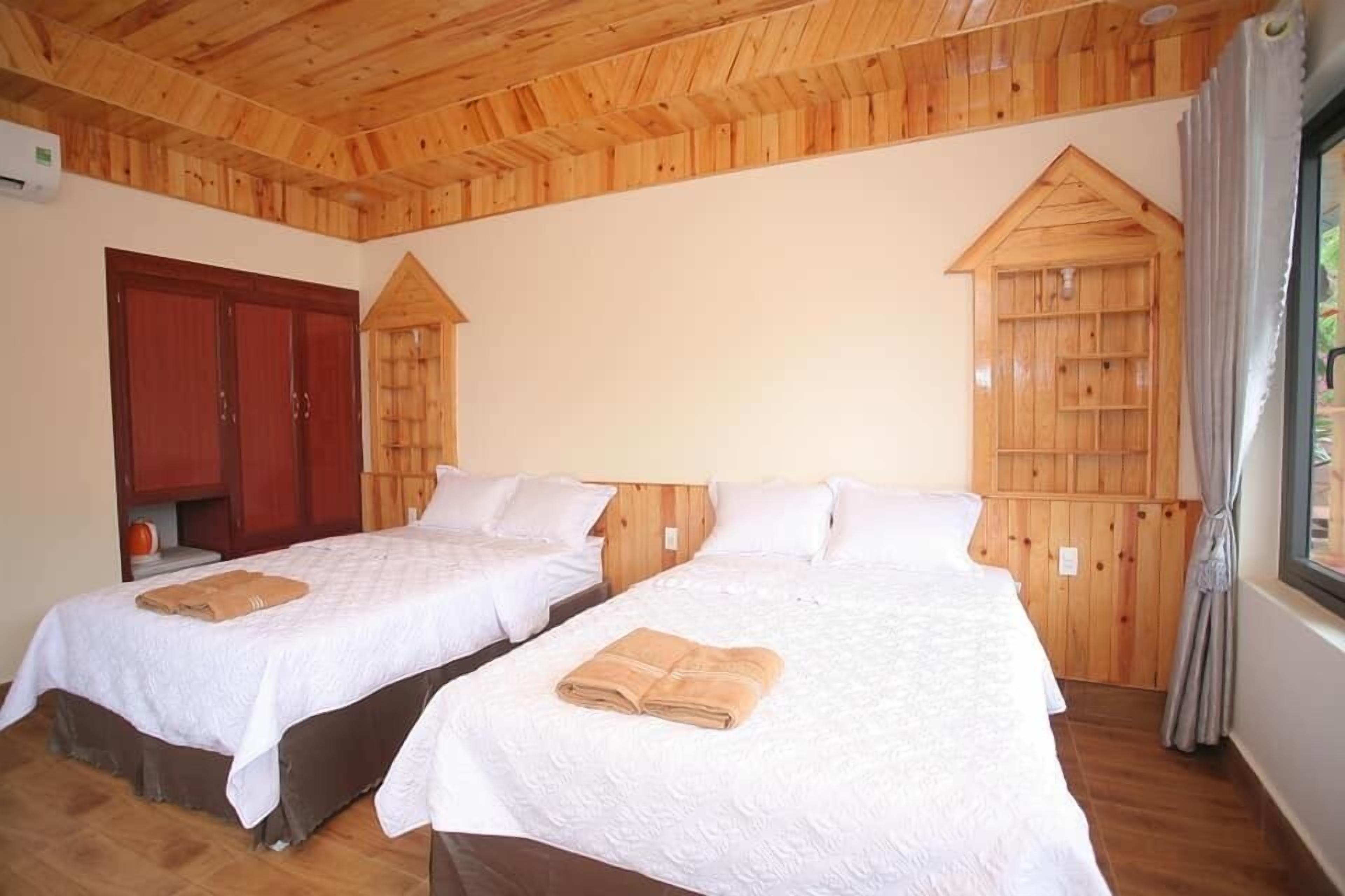 Two single beds with white linens and brown towels, wooden ceiling, and a wooden wardrobe.