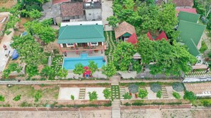 An aerial view of a residential area with a swimming pool, green-roofed houses, and a paved walkway. - Restful River Bungalow (Phong Nha)