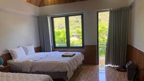 A hotel room with two beds, a wooden floor, a balcony with curtains, and a fan. - Restful River Bungalow (Phong Nha)