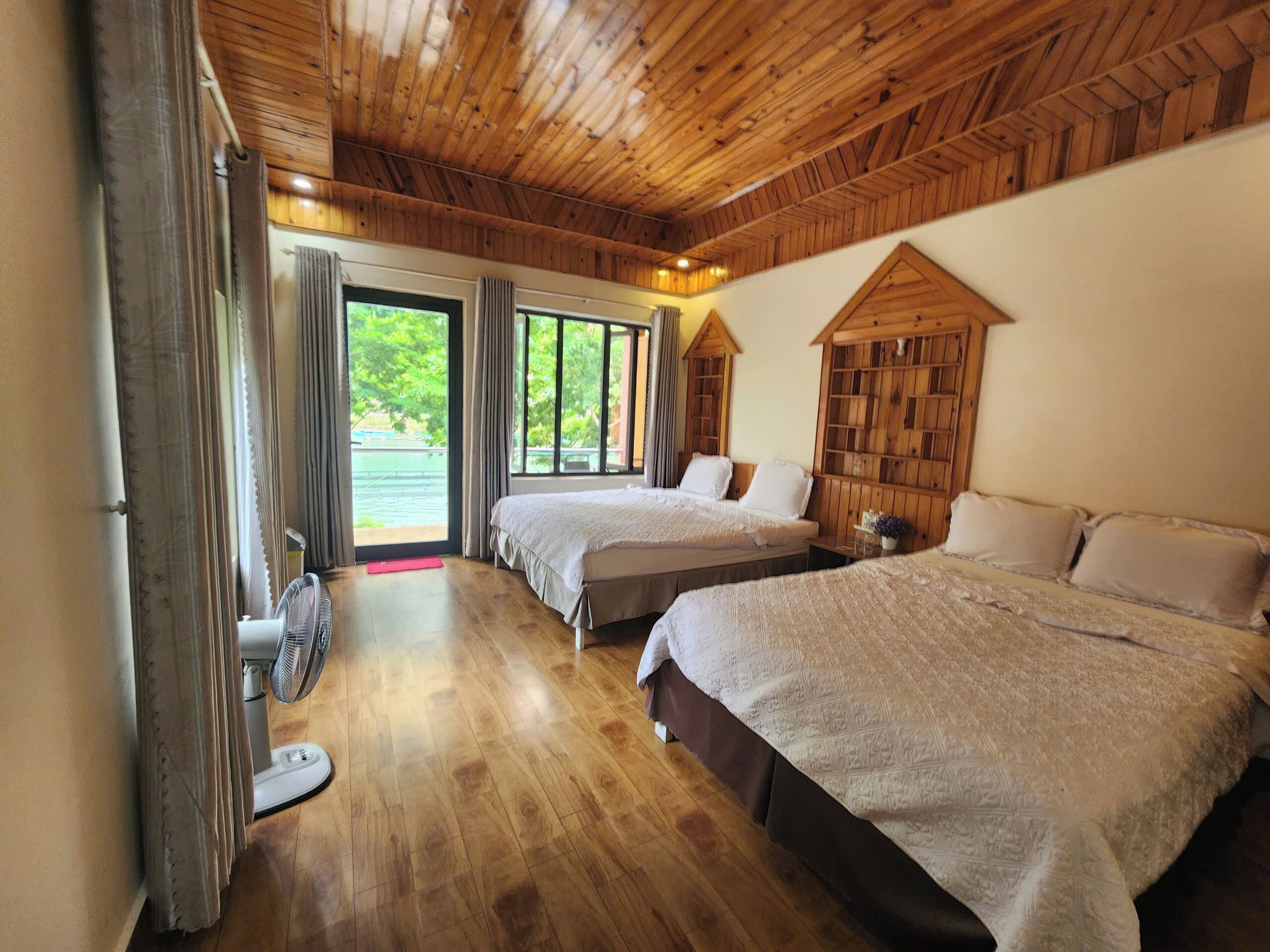 Habitación con paneles de madera, dos camas, un ventilador y vistas al exterior.