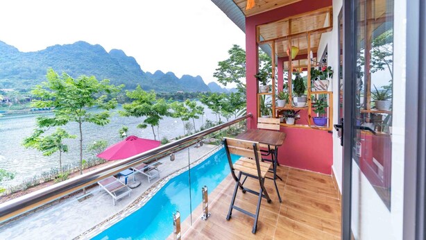 A balcony with a wooden table and chairs, overlooking a river and mountains. - Restful River Bungalow (Phong Nha)
