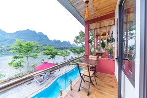 A balcony with a wooden table and chairs, overlooking a river and mountains. - Restful River Bungalow (Phong Nha)