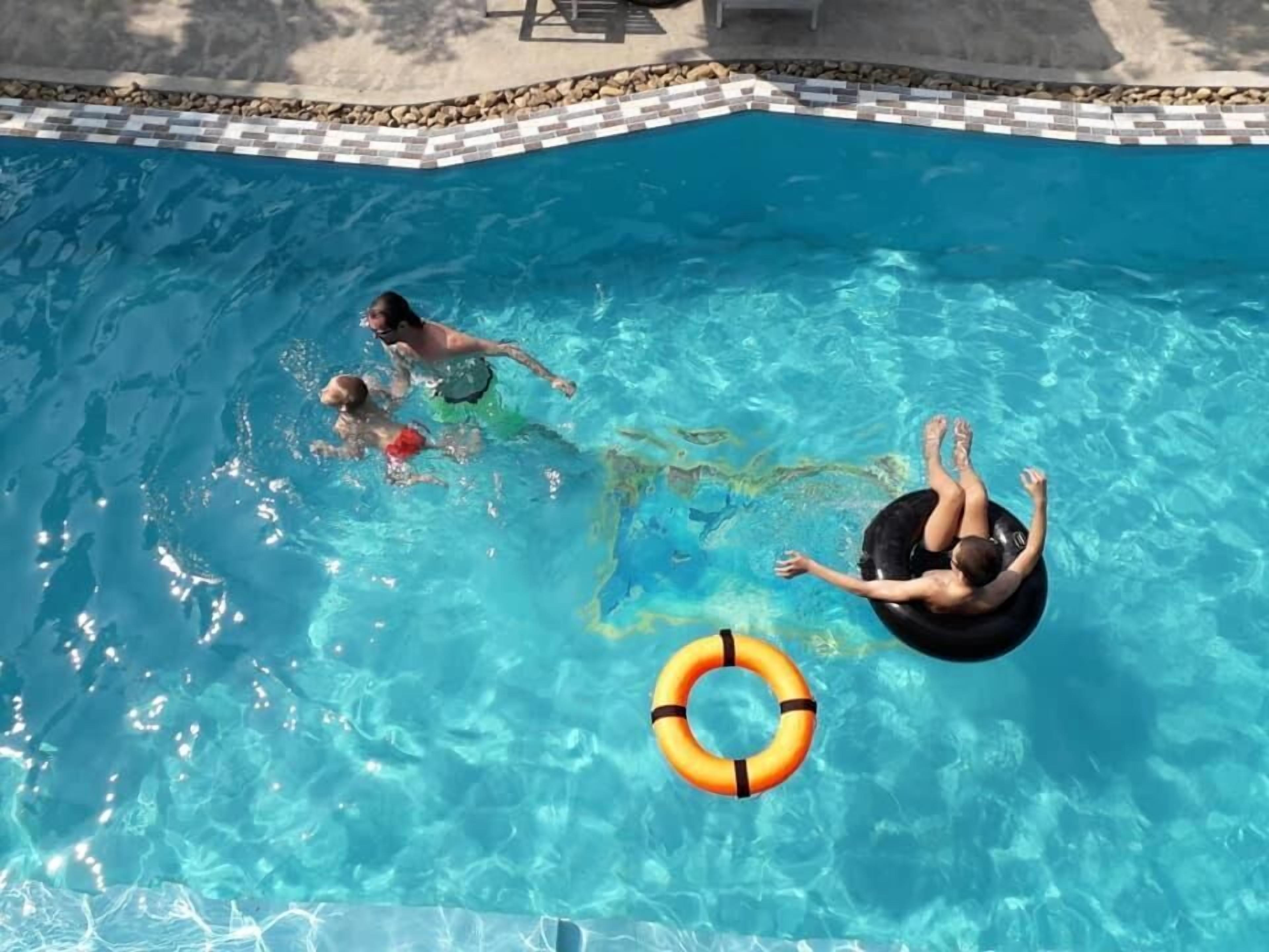 Una piscina con agua azul cristalina, borde de azulejos y un flotador.