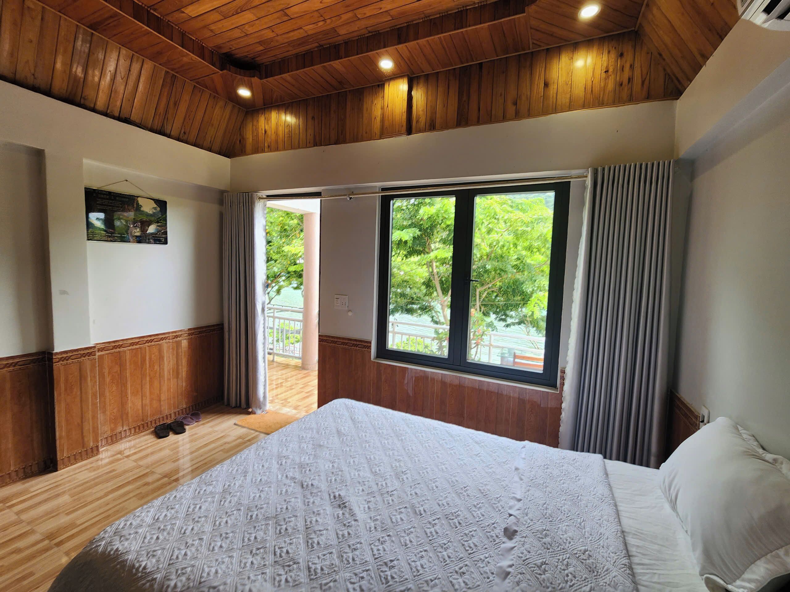 A bedroom with a large bed, wooden ceiling, and a view of greenery outside.