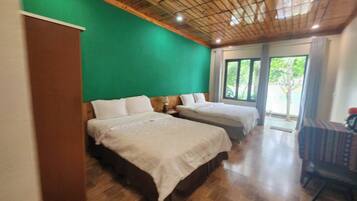 Een kamer met twee bedden, houten vloer, een groene wand en een groot raam met uitzicht op groen.
