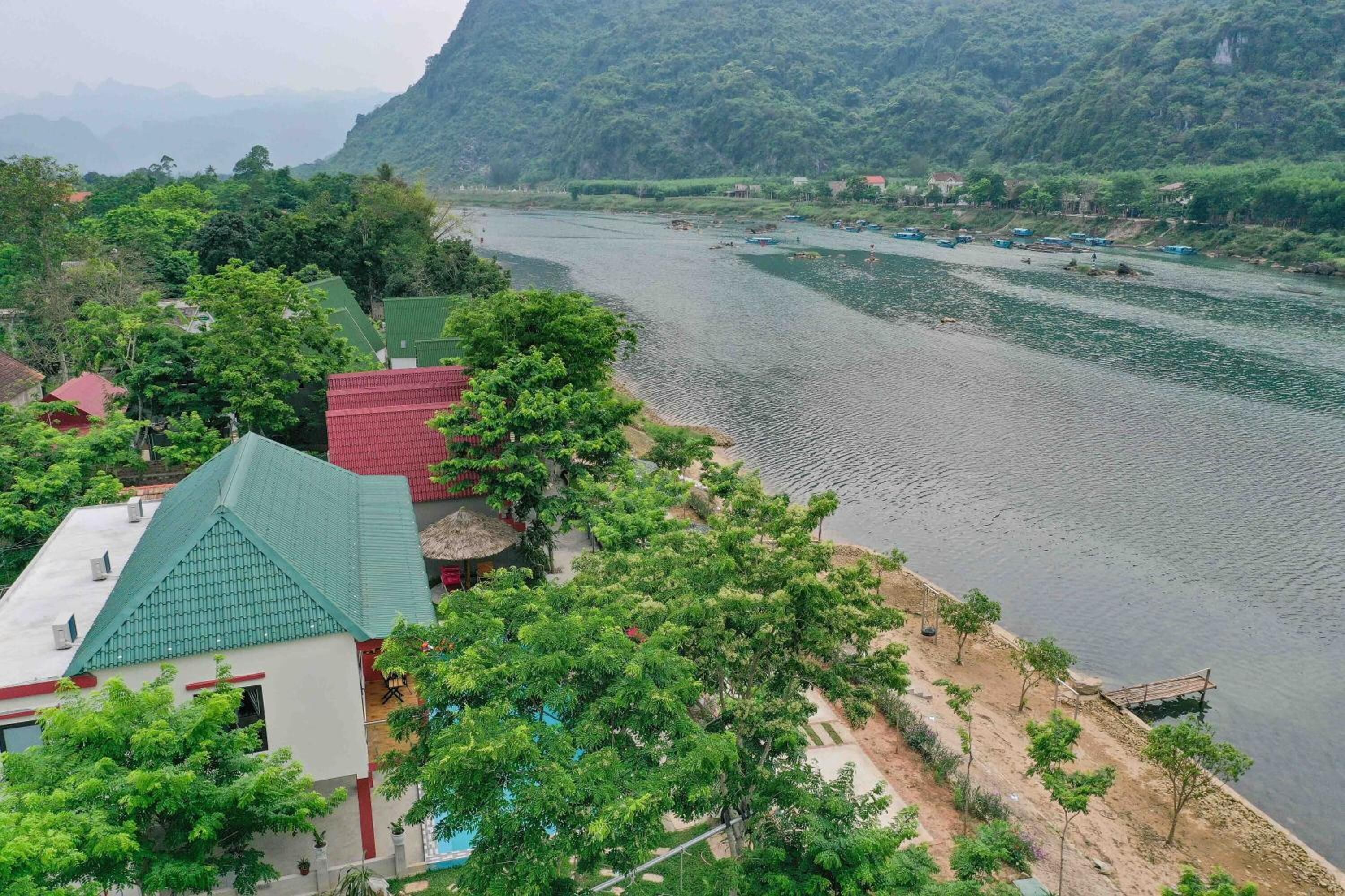 A riverside view with a building featuring a green roof, surrounded by lush greenery and a river with boats.