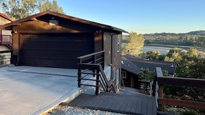 Un garage en bois avec une porte sombre, une terrasse en bois et, au loin, une vue sur une rivière et une forêt.