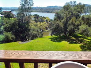 A view from a balcony overlooking a lake, surrounded by trees and a grassy area. - Lakefront Nacimiento home close to West Ramp, Internet, Dish, Pet Friendly too (Lake Nacimiento)
