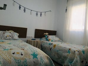 Two single beds with patterned duvets, a small table, and a decorative fish mobile above.