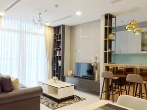 A modern living room with a sofa, coffee table, TV, bookshelf, and kitchen area with bar stools. - Saffron Casa (Ho Chi Minh City)