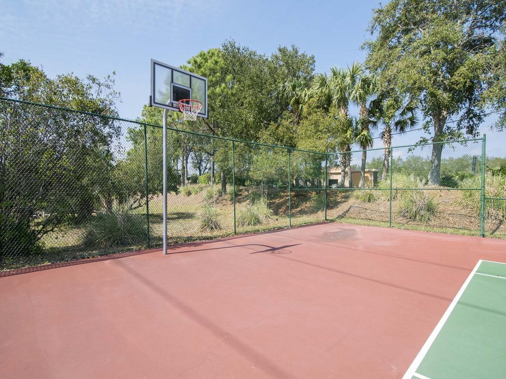 Una cancha de baloncesto al aire libre con valla de alambre, árboles y cielo despejado.