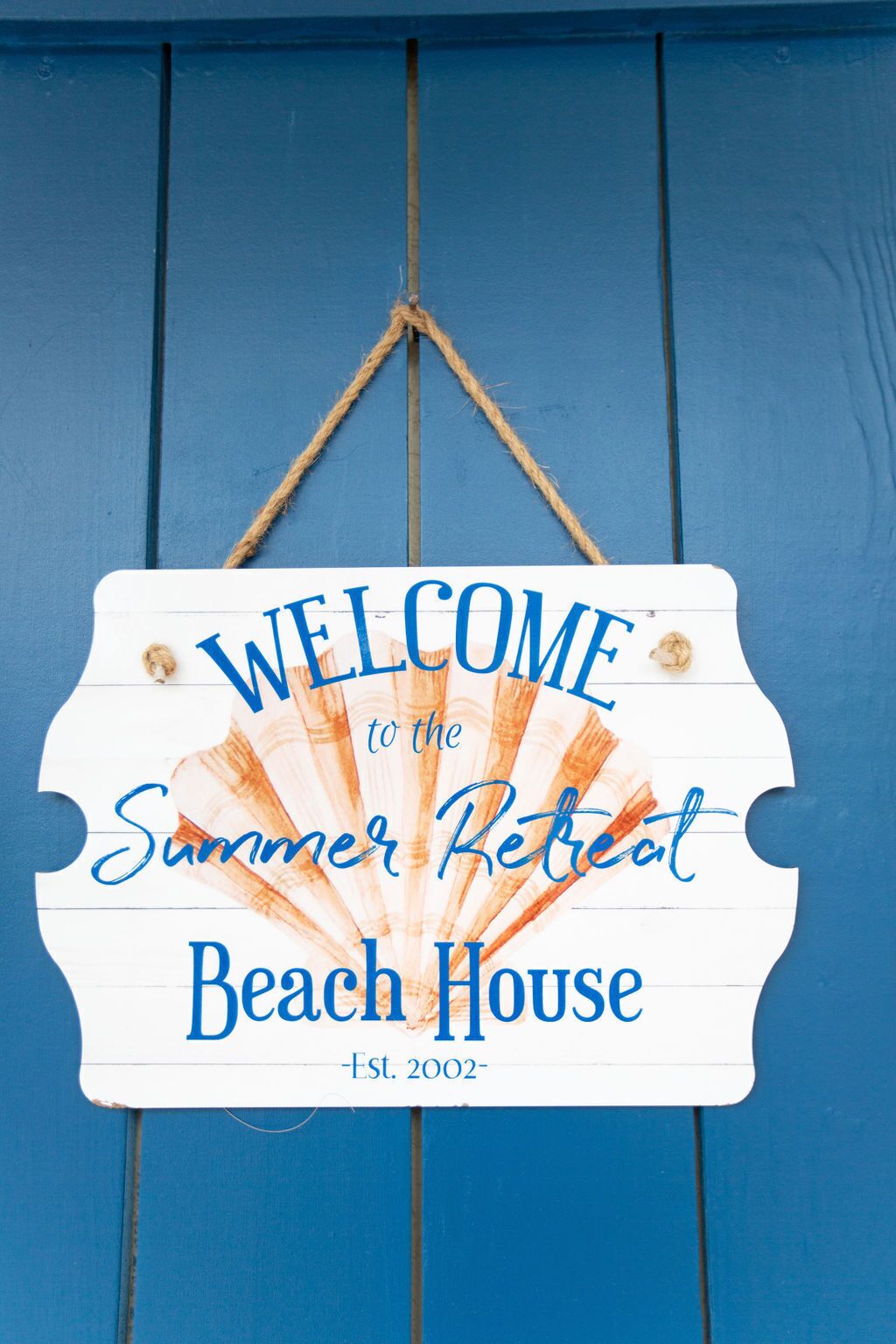 A welcome sign for the Summer Retreat Beach House, established in 2002, hanging on a blue wooden door.