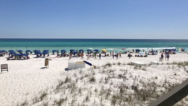 A beach with white sand, clear blue water, and numerous umbrellas.
