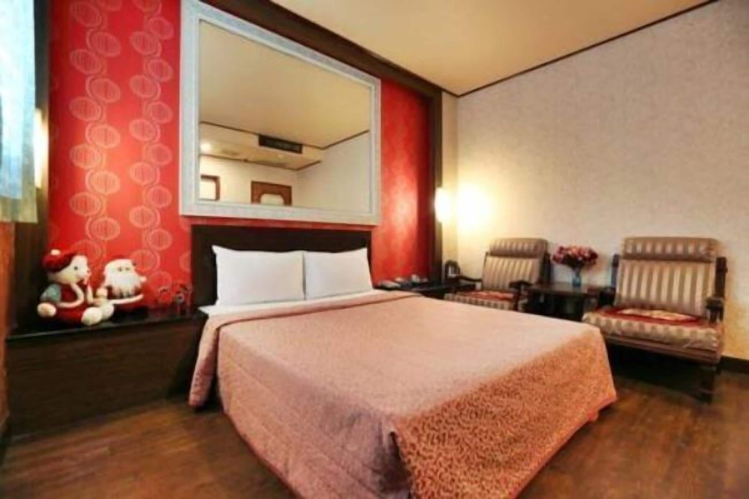 Une chambre d’hôtel avec un grand lit, deux fauteuils, une table de chevet et un miroir.
