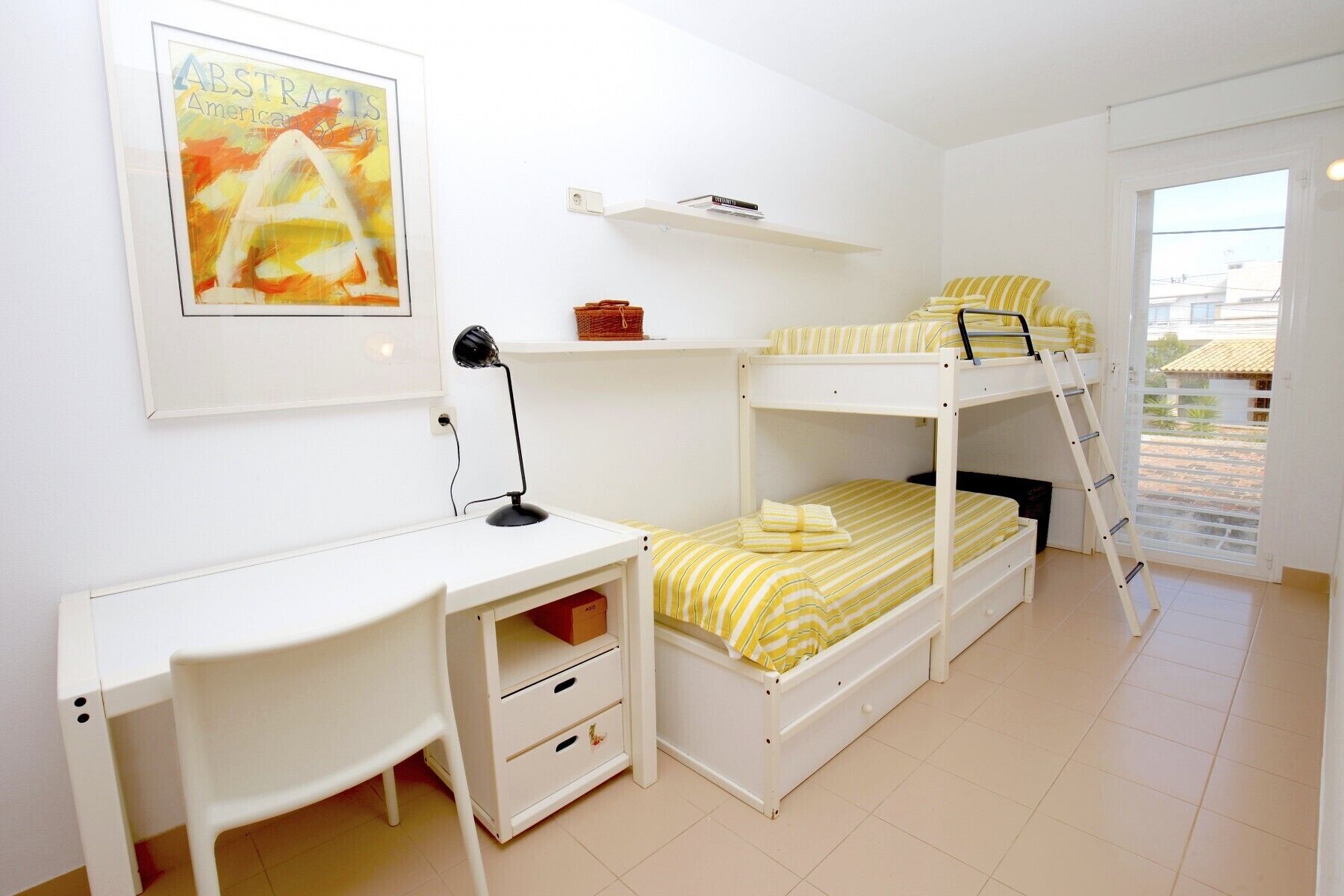 A room with bunk beds, a desk, a chair, a lamp, and a framed picture on the wall.