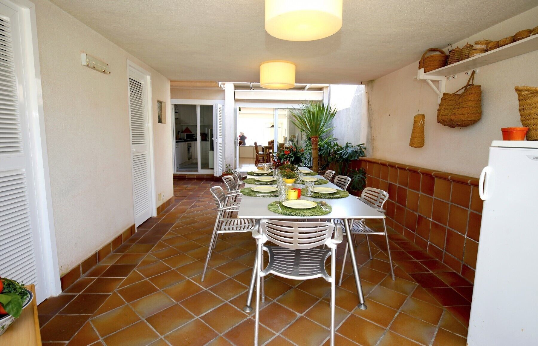 A dining area with a long table set for six, surrounded by chairs, and a kitchen area visible in the background.