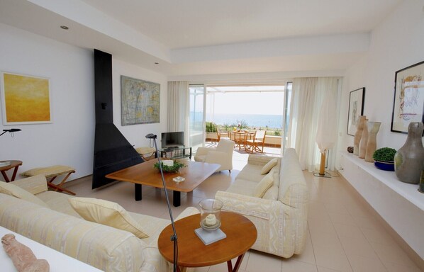 Un salon spacieux avec un grand canapé, une table basse et un téléviseur. Il y a un balcon avec vue sur la mer.