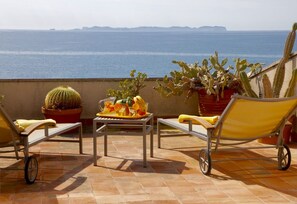 A terrace with two yellow chairs, a table with fruit and drinks, and potted cacti.