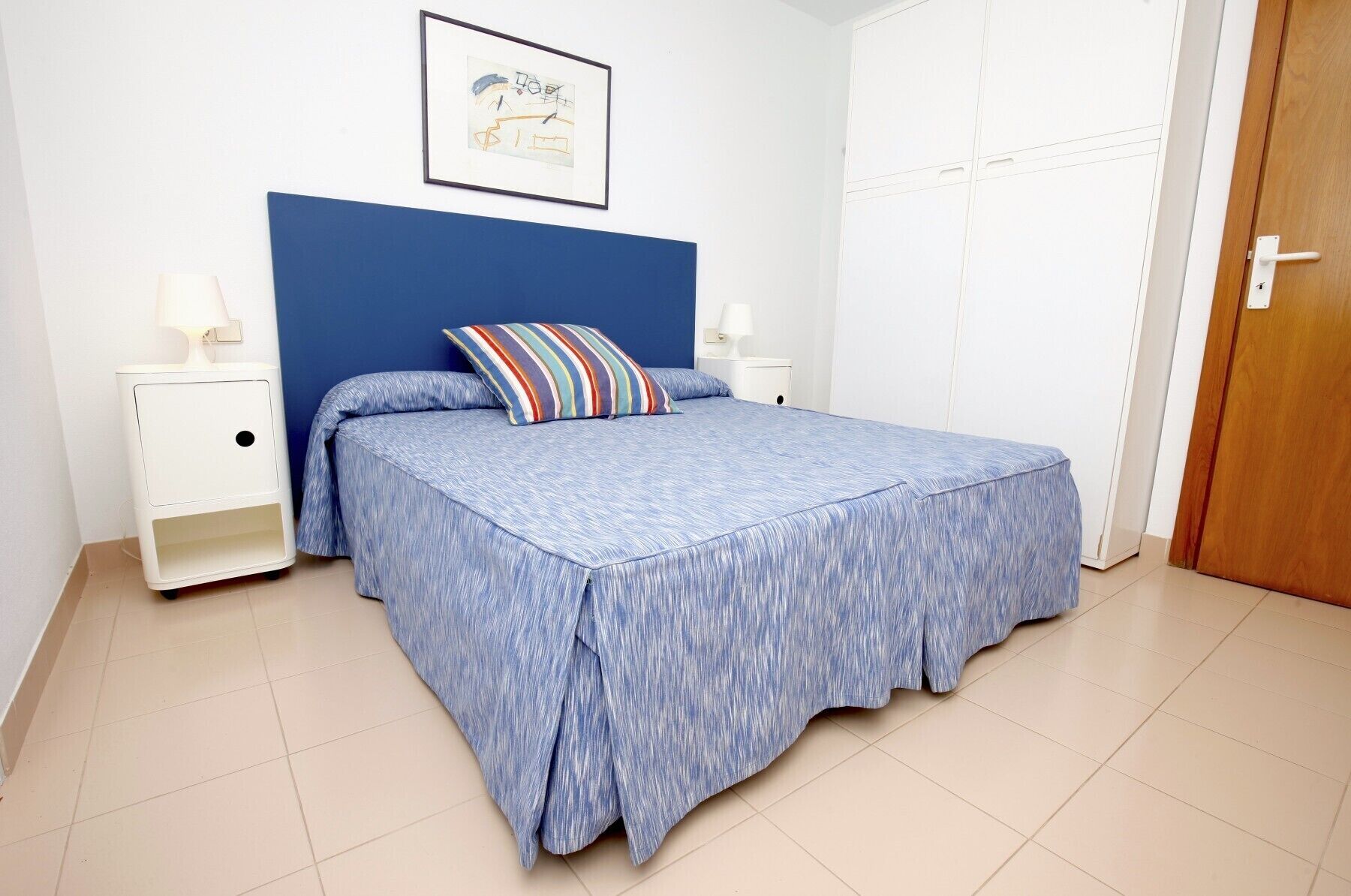 Une chambre à coucher comprenant un lit, deux tables de chevet, une commode, une porte et un tableau accroché au mur.