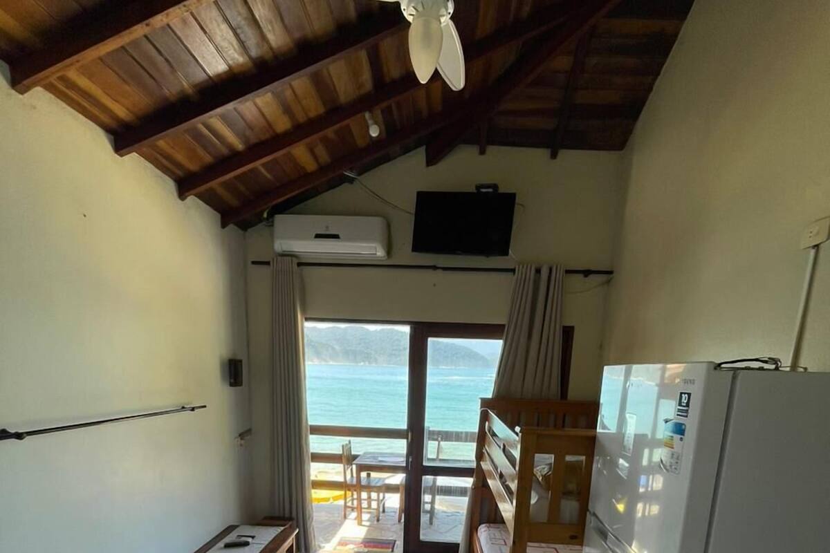 A room with a bed, a desk, a refrigerator, and a view of the sea.