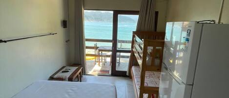 A room with a bed, a desk, a refrigerator, and a view of the sea.