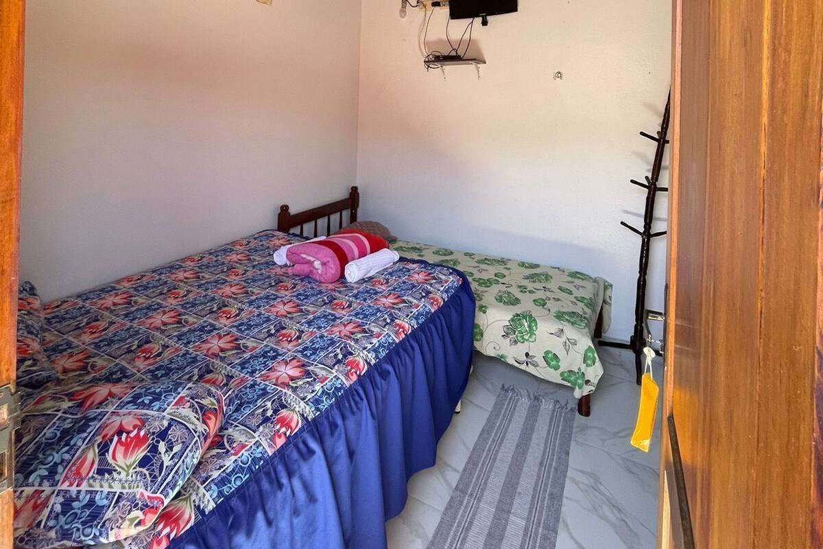 A bedroom with a bed, a smaller bed, a ceiling fan, an air conditioning unit, a TV, and a wooden door.