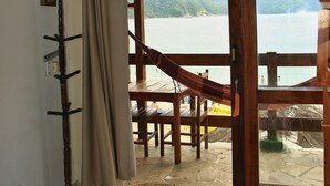 A room with a large sliding glass door leading to a deck overlooking a body of water. - Pousada Veromar (Paraty)