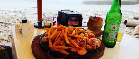 Una mesa con comida que incluye camarones y papas fritas, una botella de Heineken, una jarra de cerveza y un recipiente pequeño con salsas.