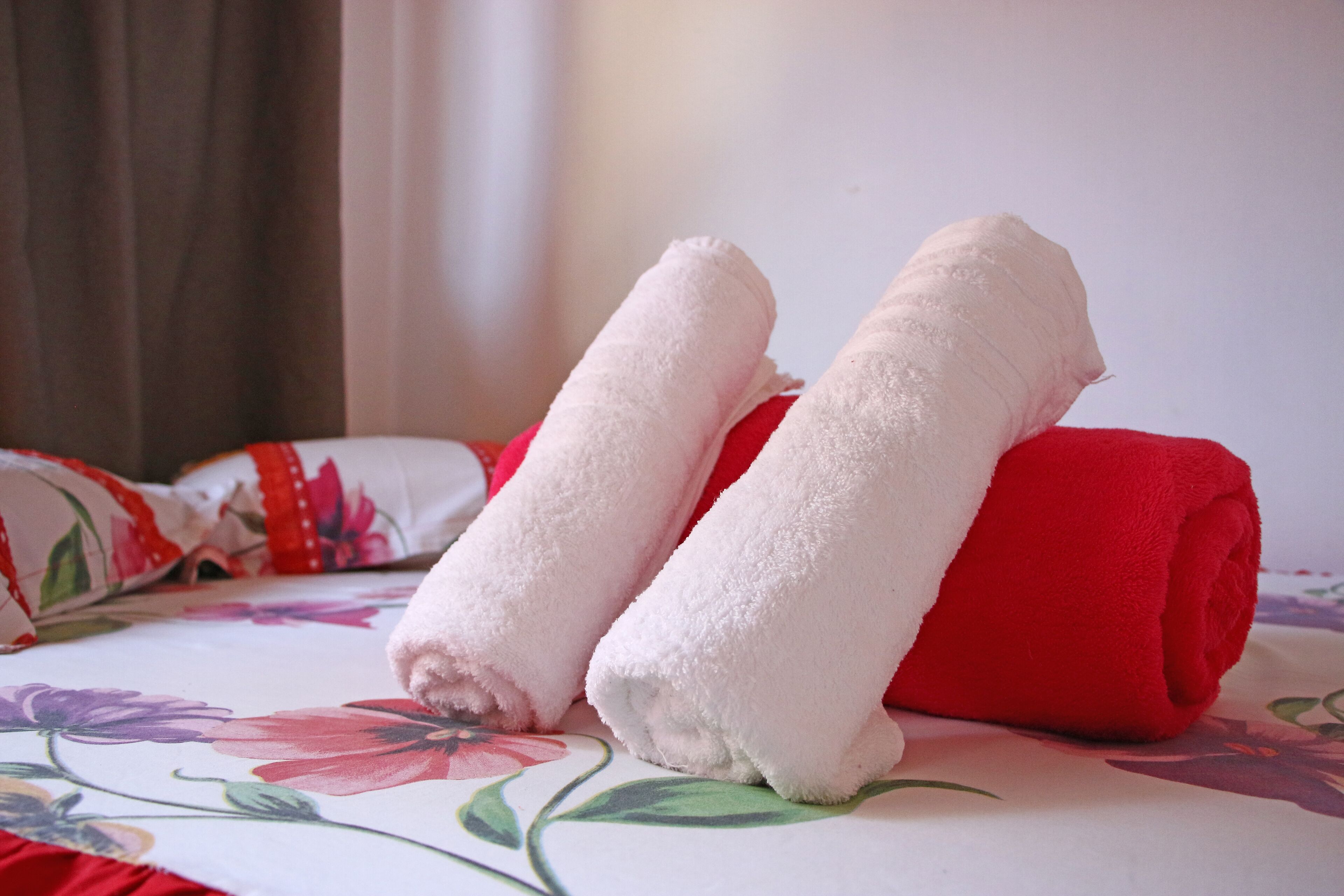 Un lit recouvert d’une couvre-lit à motifs floraux et agrémenté de deux serviettes enroulées, une blanche et une rouge.