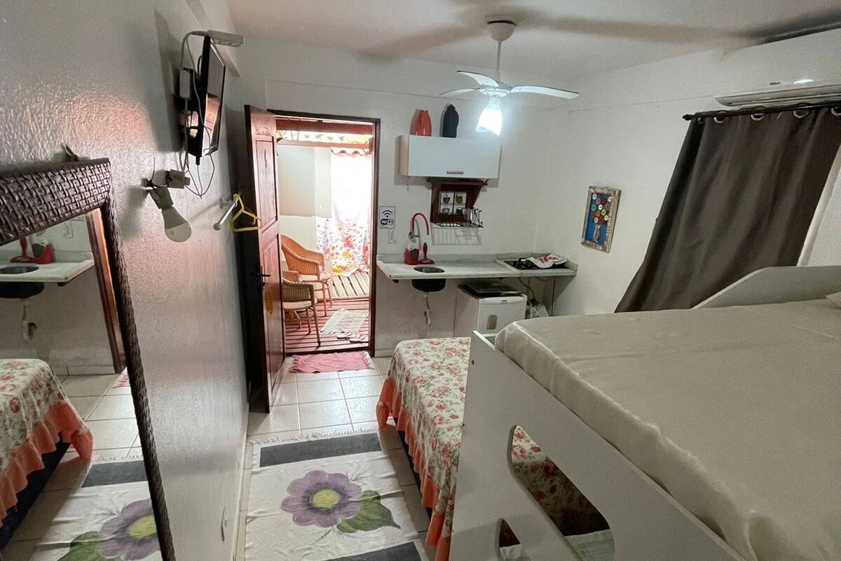 A compact room with two beds, a desk, a ceiling fan, and a small kitchenette.