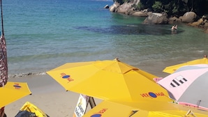 A beach with clear water, yellow umbrellas, and rocky terrain. - Pousada Veromar (Paraty)