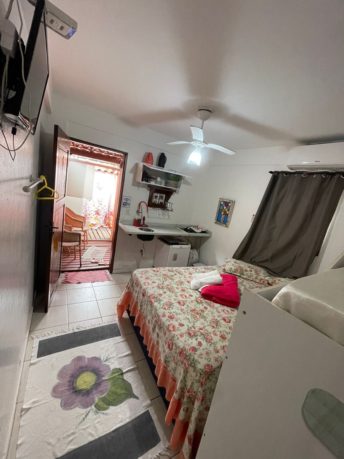 A compact bedroom with a bed, a desk, and a chair. There is a ceiling fan and a window with curtains.