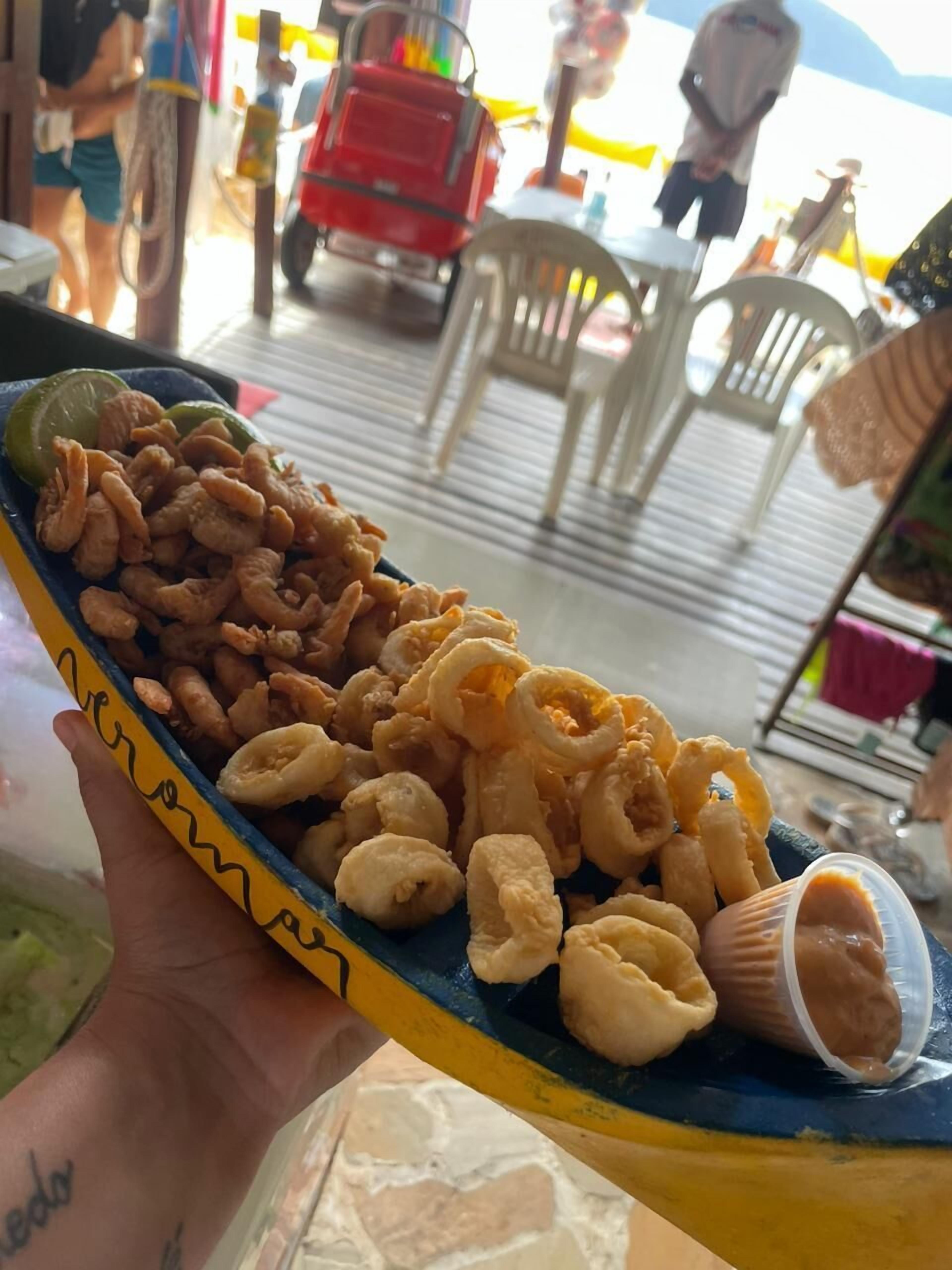 A hand holding a yellow plate with fried food and a small container of sauce.