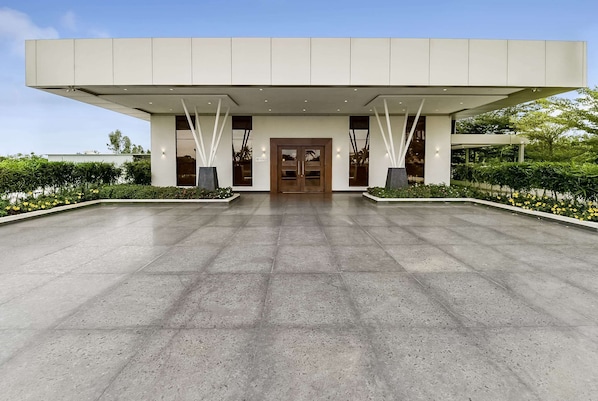 Un bâtiment moderne doté d’une grande entrée, d’un vaste espace pavé et d’un aménagement paysager symétrique.