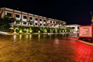 L’entrée d’un hôtel, avec un trottoir dallé, une signalétique indiquant la direction du hall d’accueil, du restaurant, du club-house et de la sortie.