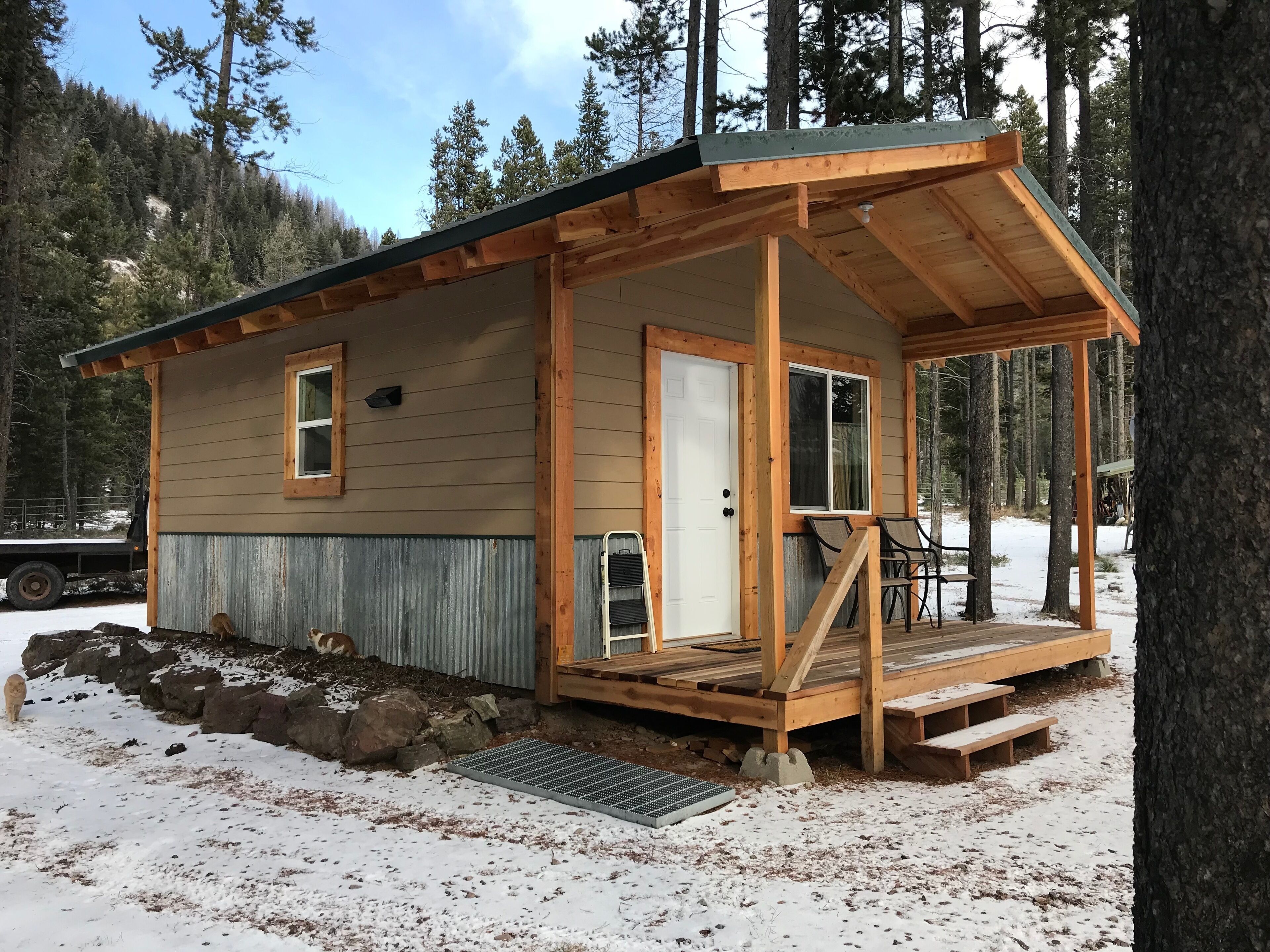 Una piccola casetta con una veranda in legno, un portico e una porta di metallo.