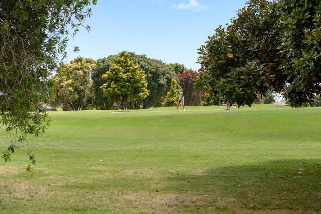 Ein Golfplatz mit gepflegtem Grün, Bäumen und blauem Himmel.