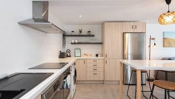 A modern kitchen with a stainless steel refrigerator, wooden cabinets, a built-in oven, and a black induction cooktop.