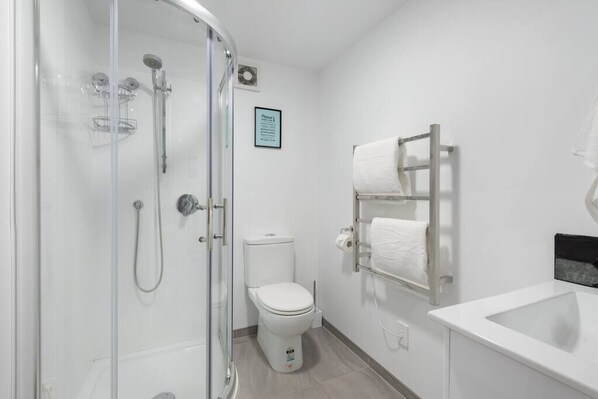 A modern bathroom with a glass-enclosed shower, a toilet, and a white sink. - The Little Blue Penguin- 2br Suite Central Mount Maunganui (Mount Maunganui)