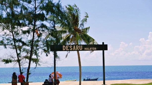 Escena de playa con un letrero que dice 'DESARU MALAYSIA'.