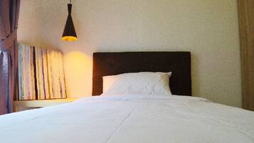 A neatly made bed with white linens, a dark headboard, and a single hanging lamp providing light.