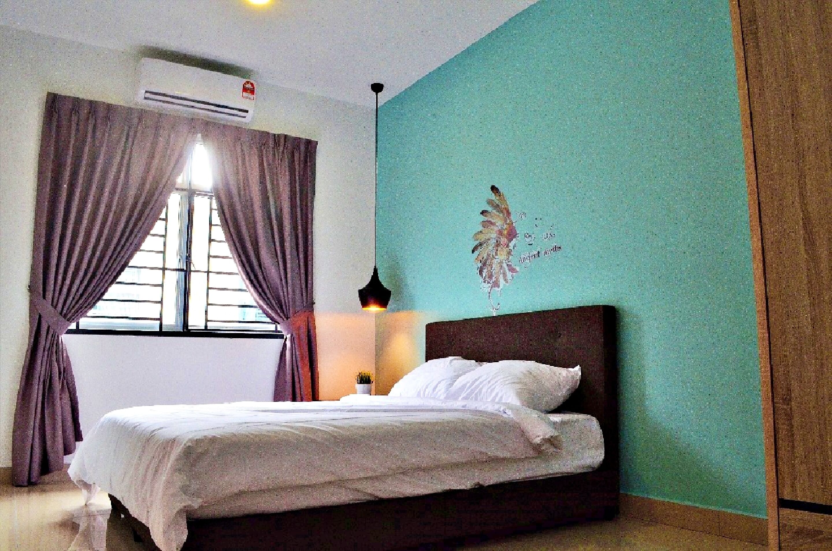 A bedroom with a bed, curtains, an air conditioning unit, a wall decoration, and a nightstand with a lamp.