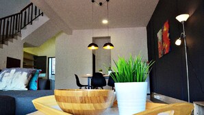Una sala de estar moderna con una mesa de centro de madera, una planta en maceta y un comedor al fondo.
