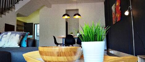 Una sala de estar moderna con una mesa de centro de madera, una planta en maceta y un comedor al fondo.