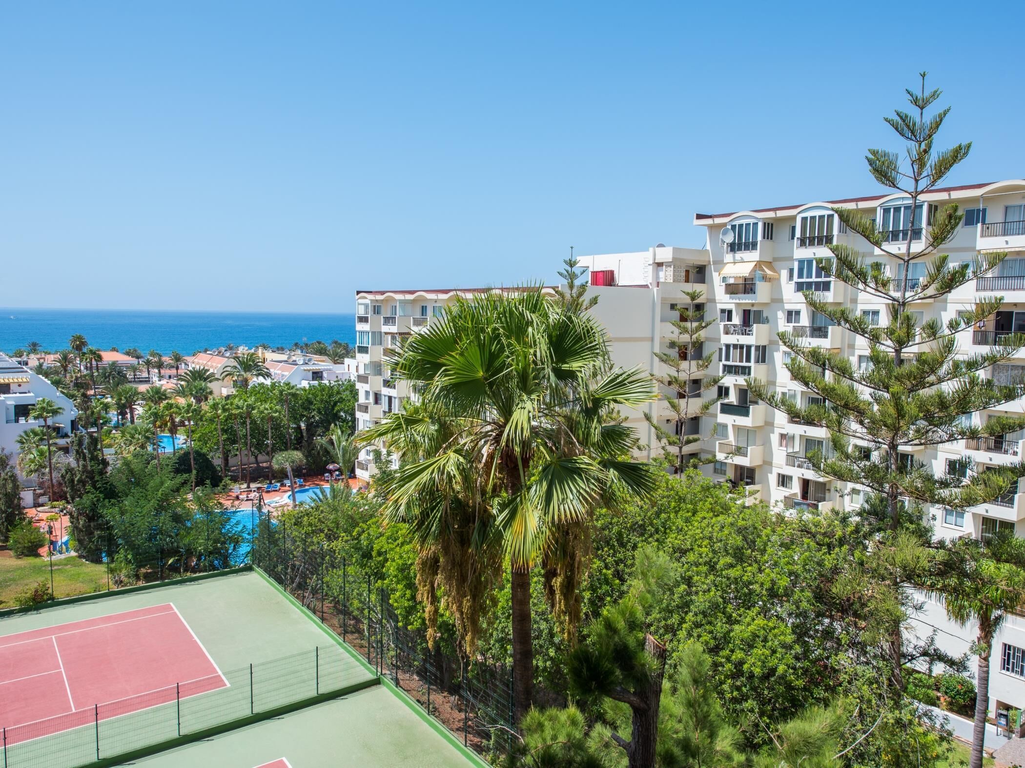 En bostadsbyggnad med flera balkonger, en tennisbana och ett poolområde.