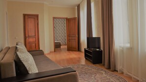 A living room with a sofa, a television, and a patterned rug. There are two doors leading to other rooms.