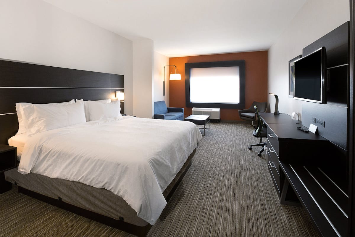 Habitación de hotel con una cama grande, un escritorio con silla, un televisor y una ventana con vista.